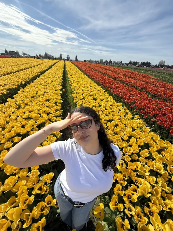 Hadar smiling in a field of red and yellow tulips, shading her eyes from the sun