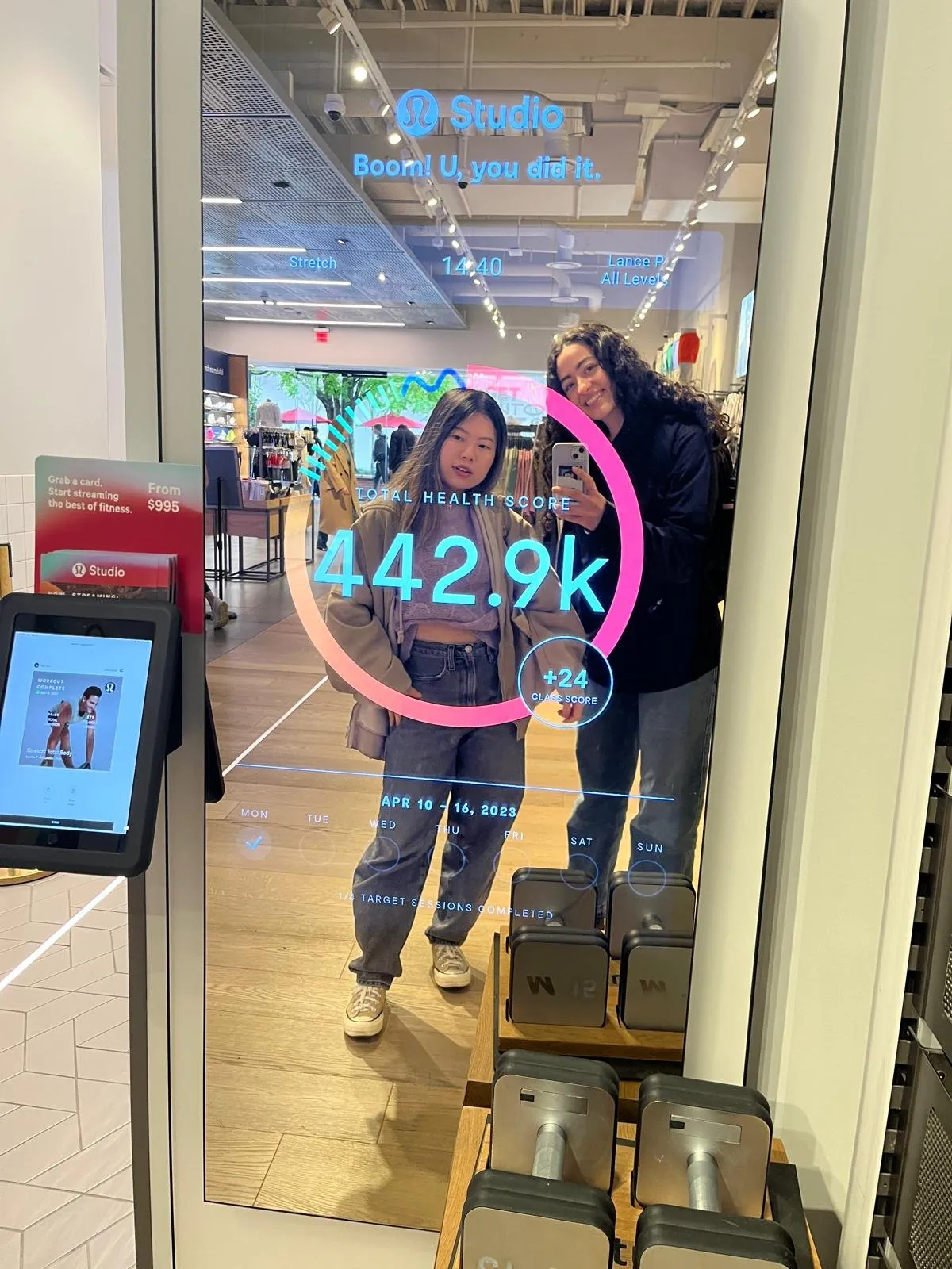Hadar and a teammate taking a photo in a Lululemon Studio smart mirror, which overlays a workout summary, a health score and weekly progress on their reflection